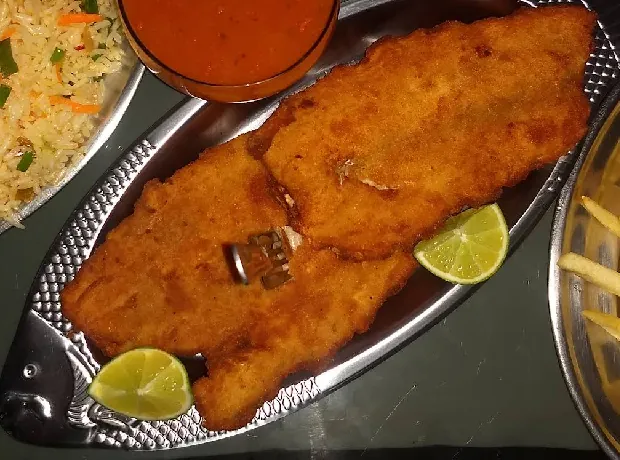 Dois filés de peixe empanados e dourados sobre travessa de inox em formato de peixe, com rodelas de limão